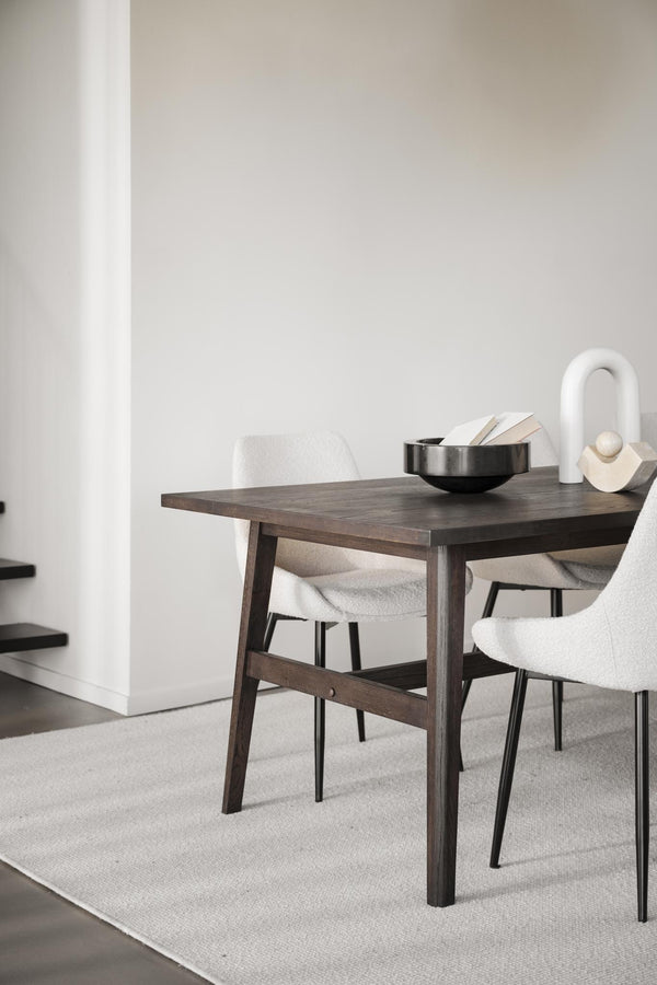 Matbord i mörkt trä med vita stoppade stolar och dekorativa föremål i minimalistisk matsal