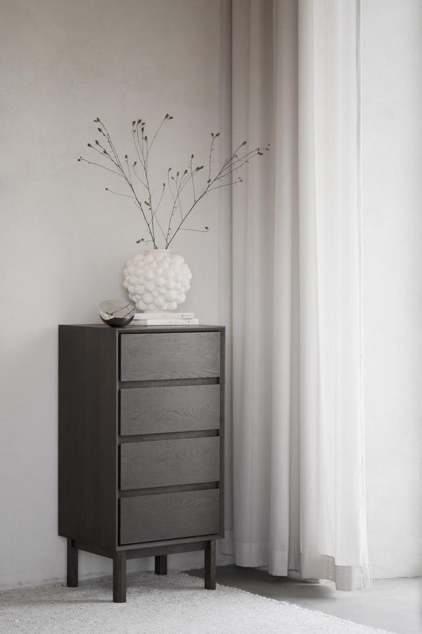Mörk träbyrå med fyra lådor och vita dekorationer i minimalistiskt sovrum med ljusa gardiner