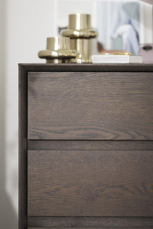 Byrå i mörkt trä med två lådor och dekorativa föremål på toppen i modern skandinavisk stil