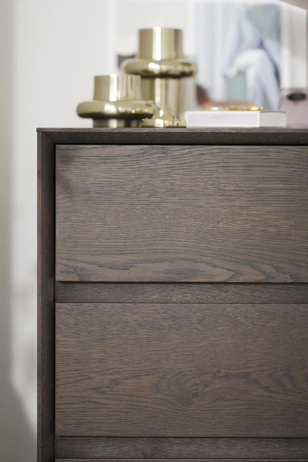 Byrå i mörkt trä med två lådor och dekorativa föremål på toppen i modern skandinavisk stil