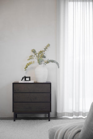 Mörk byrå med tre lådor i sovrum med vit vas och eukalyptusgrenar som dekoration
