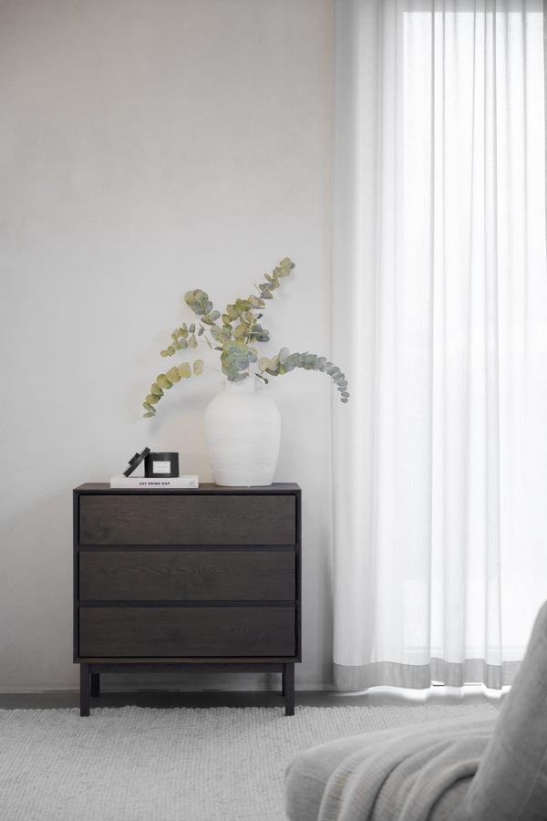 Mörk byrå med tre lådor i sovrum med vit vas och eukalyptusgrenar som dekoration