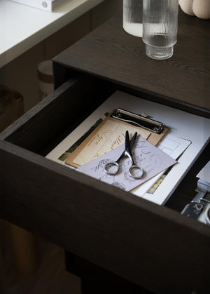 Öppen låda i mörkt trä med sax, papper och clipboard - förvaring i sängbord eller skrivbord