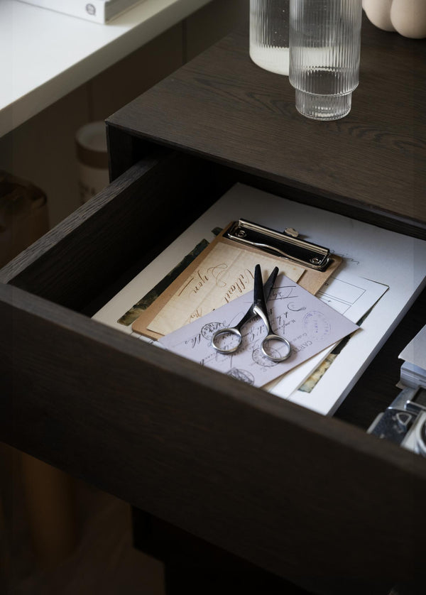 Öppen låda i mörkt trä med sax, papper och clipboard - förvaring i sängbord eller skrivbord