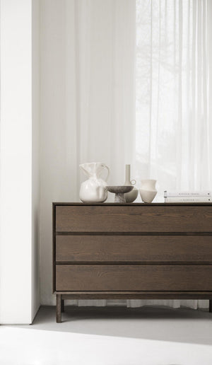 Brun träbyrå med tre lådor och dekorativa keramikvas och böcker på toppen i minimalistisk inredning