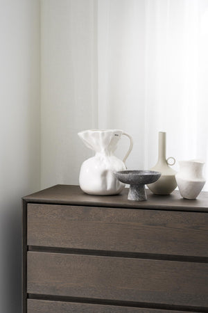 Minimalistisk byrå i mörkt trä med dekorativa vaser och skålar i vitt och grått på toppen