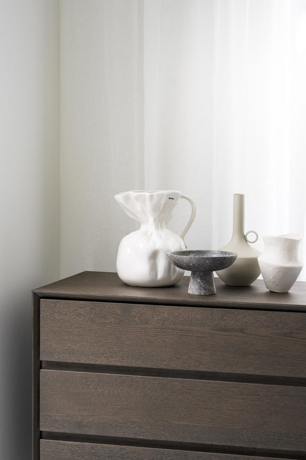 Minimalistisk byrå i mörkt trä med dekorativa vaser och skålar i vitt och grått på toppen