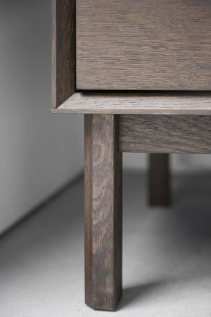 Närbild på möbelben och hörn av träbord med grå yta och mörkbrun träram i modern design