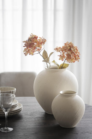 Cremefärgade keramikvasor med torkade blommor på matbord med tallrikar och glas