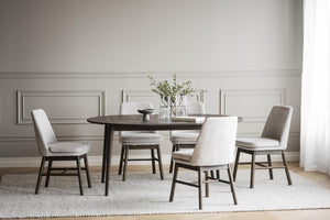 Matgrupp med runt träbord och sex beige stoppade stolar i ljus matsal med vit väggpanel