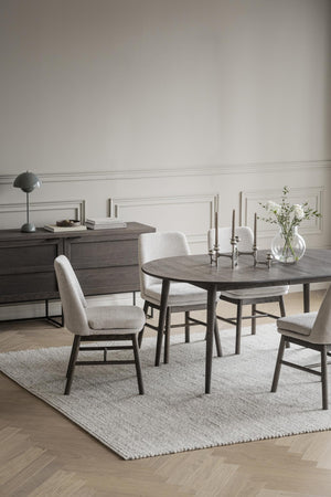 Rund matbord i mörkgrått trä med matchande stolar i ljusgrå klädsel, stilren skandinavisk design för matsalen