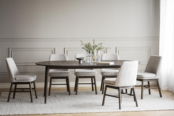 Matgrupp med ovalt mörkt träbord och sex ljusgrå stoppade stolar i modern skandinavisk design