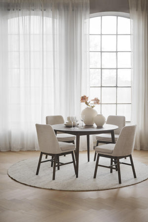 Rund matgrupp med fyra beige stolar vid stort fönster med vita gardiner i ljust matrum