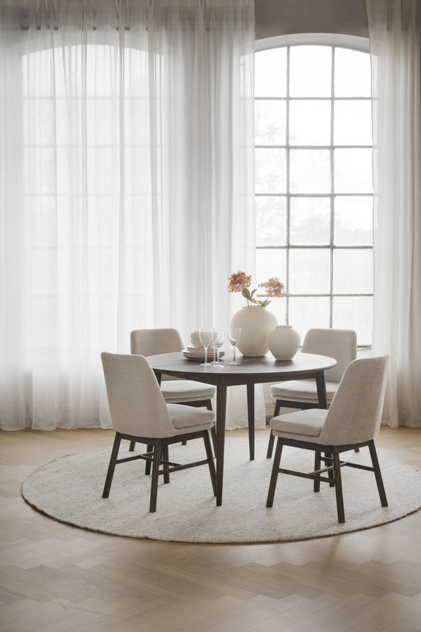 Rund matgrupp med fyra beige stolar vid stort fönster med vita gardiner i ljust matrum