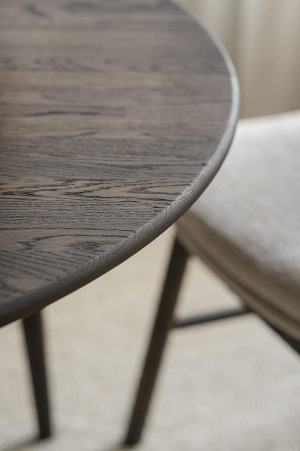 Närbild på rund träbordsskiva med grå yta och rundad kant, stående på metallben