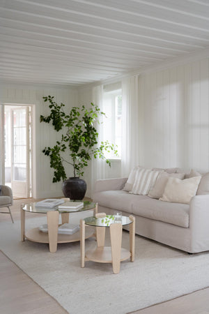 Ljust vardagsrum med beige soffa, runda soffbord i trä med glasskiva och gröna växter vid vit panel