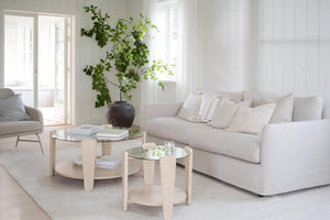 Ljust vardagsrum med beige soffa, runda soffbord i trä och glas, samt grön växt i vas