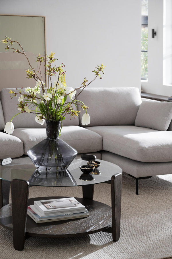 Modernt soffbord i mörkt trä med glasskiva, dekorerat med vas och böcker i ljust vardagsrum