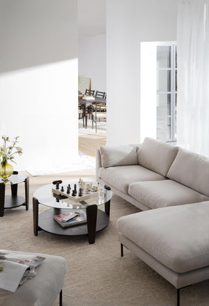 Ljust vardagsrum med beige soffa, runt soffbord i glas och trä, schackspel och minimalistisk inredning