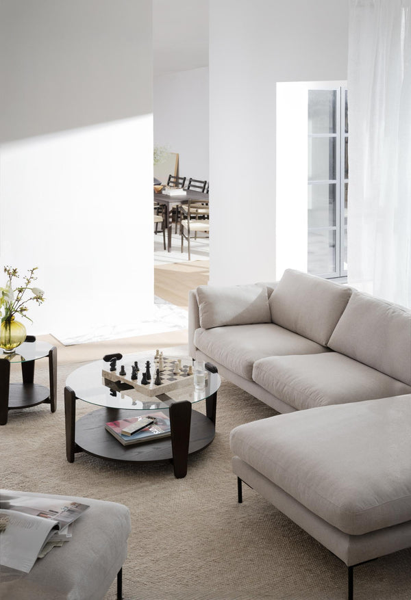 Ljust vardagsrum med beige soffa, runt soffbord i glas och trä, schackspel och minimalistisk inredning