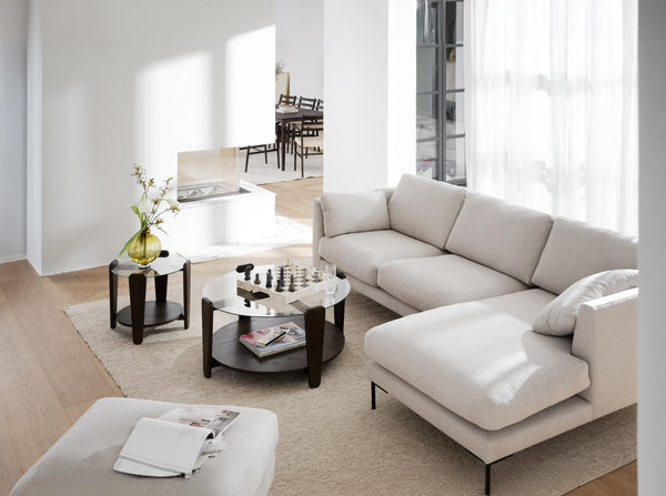 Ljus vardagsrumsinteriör med beige hörnsoffa, runda soffbord i marmor och trä, minimalistisk inredning