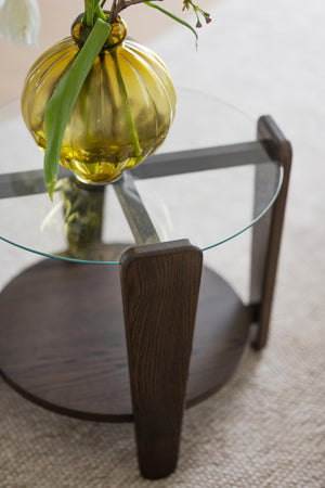 Runt soffbord i mörkt trä med glasskiva och gul glasvas med gröna växter