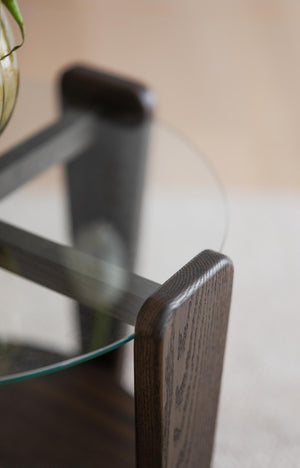 Närbild på mörkbrun trädetalj med rundad kant på glasmöbel mot ljus vägg