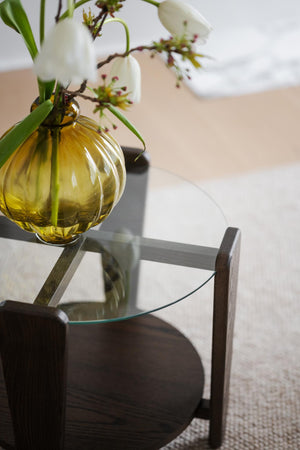 Gul glasvas med blommor på soffbord med glasskiva och mörkt trä