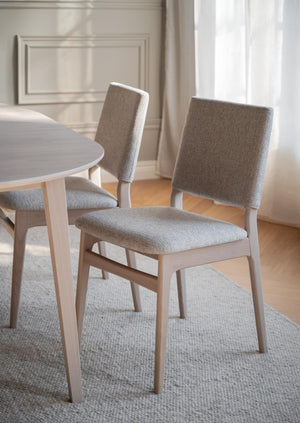 Ljusa matsalsstolar med grå klädsel och träben vid runt matbord i modern skandinavisk inredning