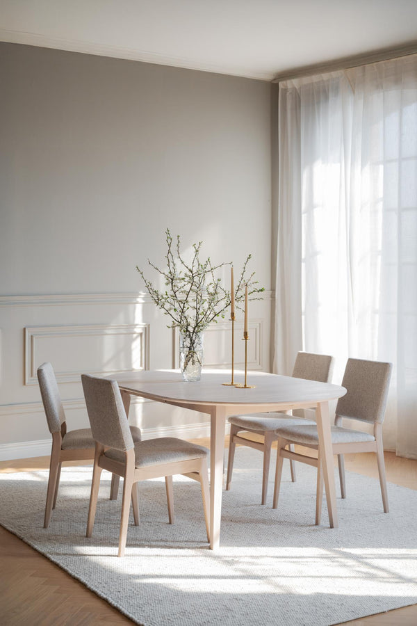 Ljus matgrupp i trä med fyra stoppade stolar, runt bord och minimalistisk skandinavisk design