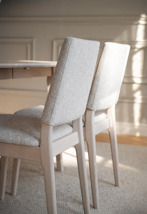 Vita stoppad matstolar med ljust trä vid matbord i elegant matsalsinteriör