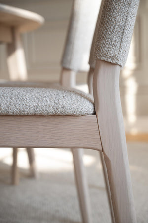 Närbild av stol med ljust trä och beige klädsel i linnelook, skandinavisk design