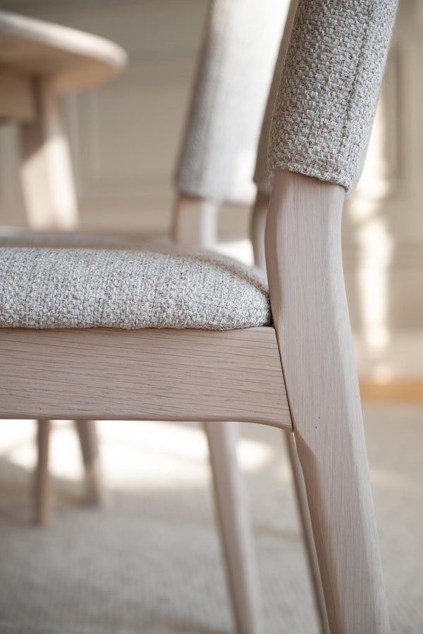 Närbild av stol med ljust trä och beige klädsel i linnelook, skandinavisk design