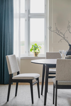 Matbord med stolar i ljus matsal med fönster, blå gardiner och minimalistisk inredning