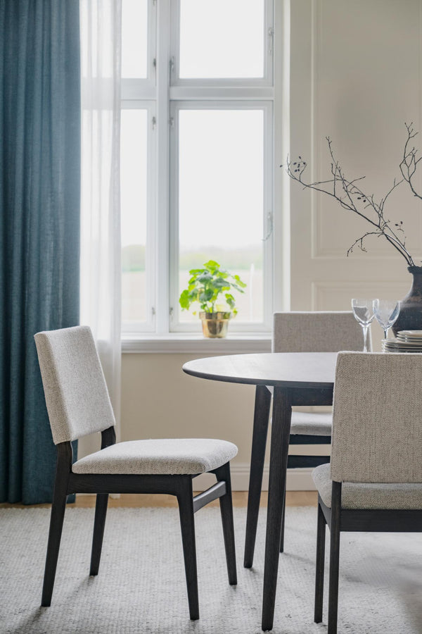 Matbord med stolar i ljus matsal med fönster, blå gardiner och minimalistisk inredning