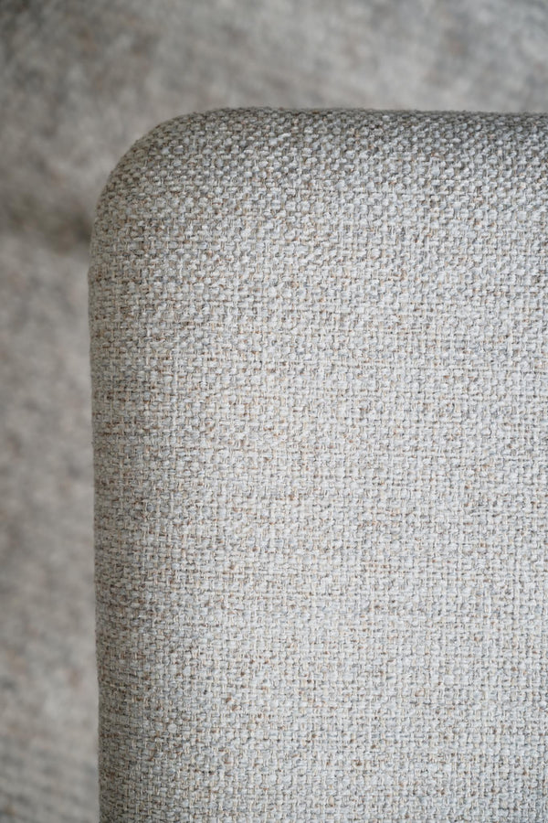 Närbild av ljusgrå möbel med tygklädsel i strukturerad vävd textil mot neutral bakgrund