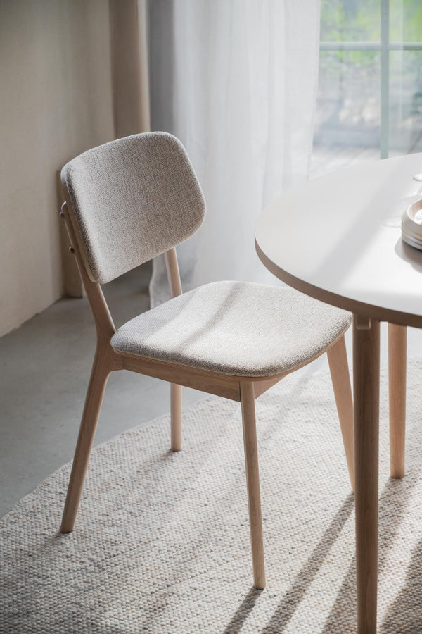 Stoppad matstol i beige tyg med träben i ljust trä, placerad vid runt matbord i modern skandinavisk stil