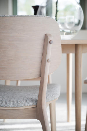 Närbild på ljus trästol med rundad rygg och grå stoppning, skandinavisk design