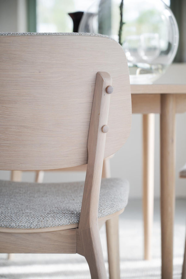 Närbild på ljus trästol med rundad rygg och grå stoppning, skandinavisk design