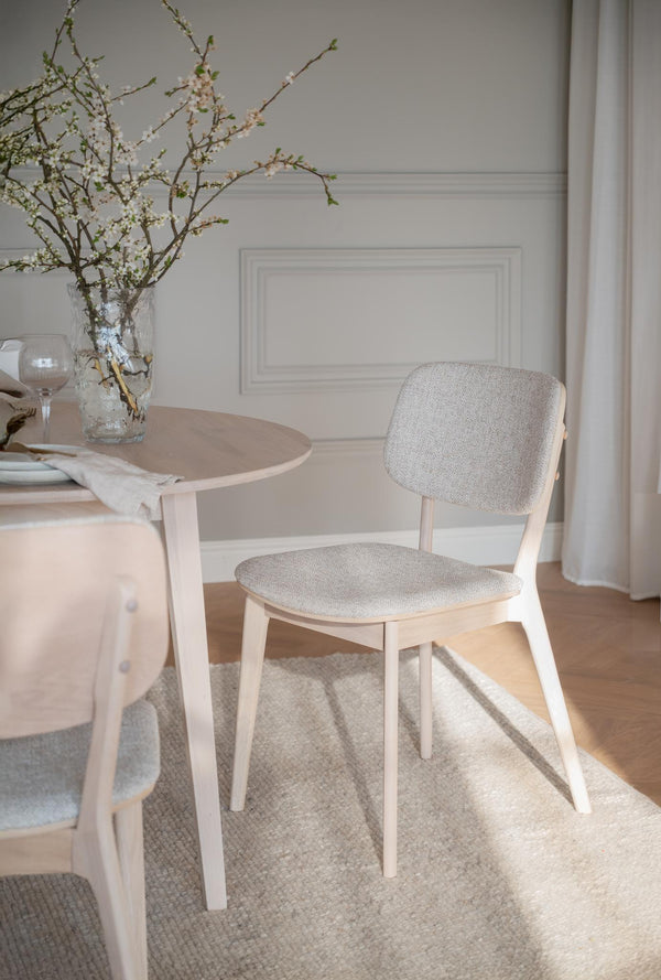 Ljus matstol med stoppad sits och rygg i beige tyg vid runt matbord med blomvas