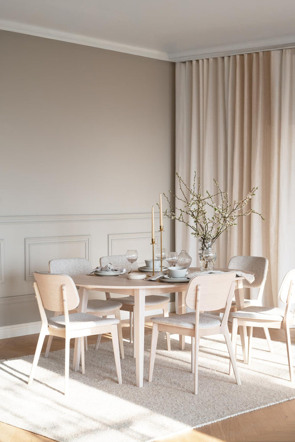 Rund matbord i ljust trä med matchande stolar i skandinavisk stil, dukad med tallrikar och vas med blomster