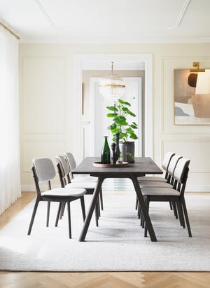 Matbord i mörkbejsat trä med sex stolar i grått tyg i elegant matsal med ljusa väggar