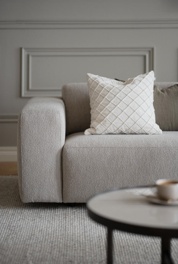 Beige bouclésofa med dekorativ vit och beige rutig kudde i modernt vardagsrum