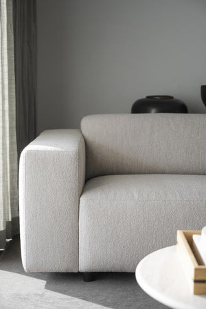 Beige boucléfåtölj med kubisk design och mjuk klädsel i ljust vardagsrum med grå vägg