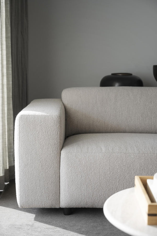 Beige boucléfåtölj med kubisk design och mjuk klädsel i ljust vardagsrum med grå vägg