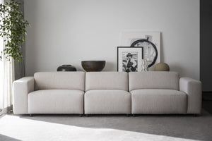 Beige modulsoffa med tre sittplatser i vardagsrum med dekorativa krukor och tavlor