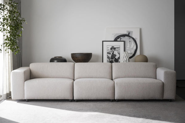 Beige modulsoffa med tre sittplatser i vardagsrum med dekorativa krukor och tavlor