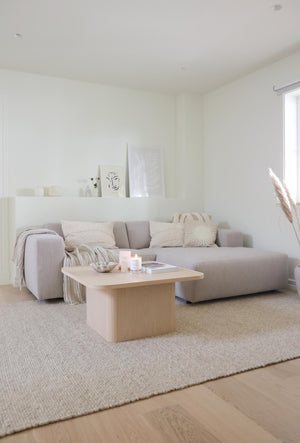 Minimalistisk vardagsrum med grå soffa, ljust soffbord i trä och beige textilier i skandinavisk stil