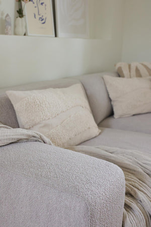 Ljusgrå soffa med kuddar i beige och vitt, närbild på mjuk bouclé-klädsel och textilier i vardagsrum