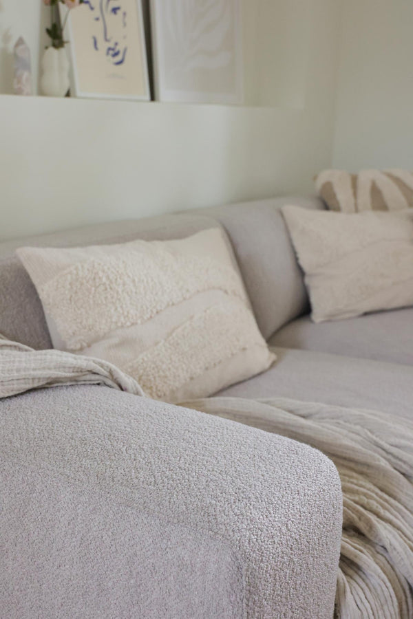 Ljusgrå soffa med kuddar i beige och vitt, närbild på mjuk bouclé-klädsel och textilier i vardagsrum